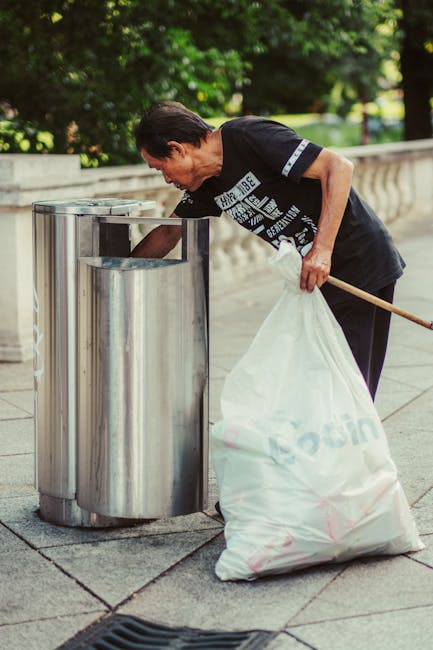 Three large black plastic rubbish bags, somewhat crumpled and tied at the top, are placed on the pavement near a black metal fence with vertical bars. The bags appear to contain miscellaneous waste an